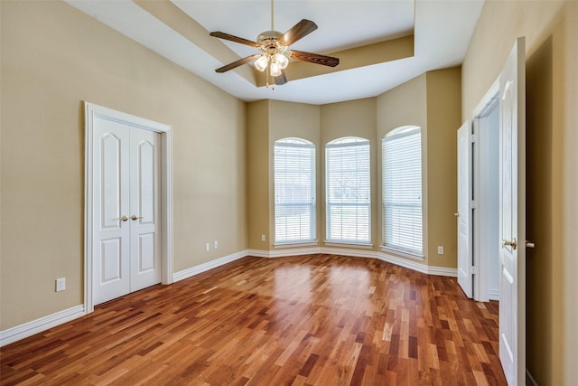 spare room with a raised ceiling, wood finished floors, a ceiling fan, and baseboards