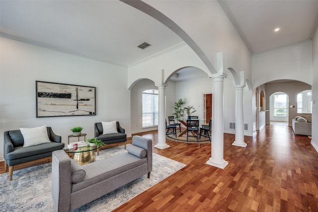 living area featuring visible vents, arched walkways, ornamental molding, wood finished floors, and ornate columns