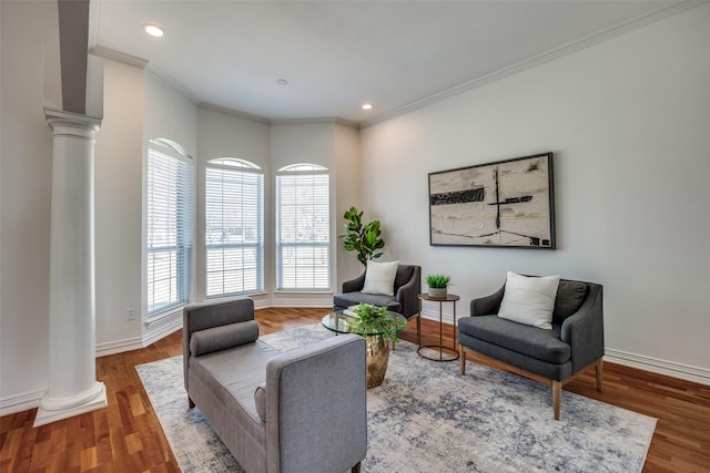 living area featuring baseboards, crown molding, ornate columns, and wood finished floors