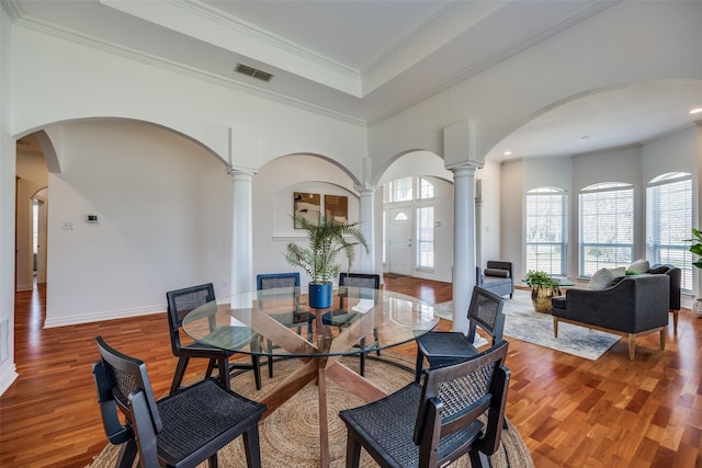 dining space with a tray ceiling, crown molding, visible vents, wood finished floors, and ornate columns