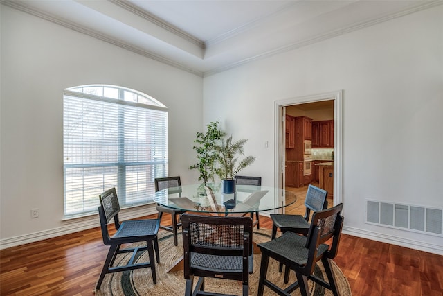 dining room featuring light wood finished floors, visible vents, a raised ceiling, and crown molding