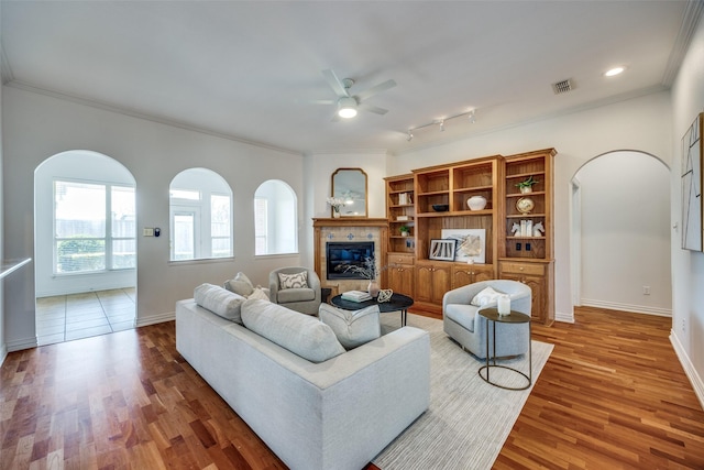 living area with visible vents, crown molding, a tiled fireplace, and wood finished floors