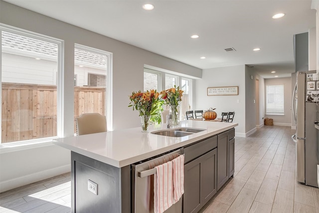 kitchen with a sink, wood tiled floor, a kitchen island with sink, and dishwasher