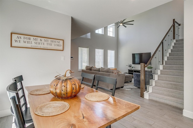 dining area featuring ceiling fan, a high ceiling, stairway, and wood finished floors