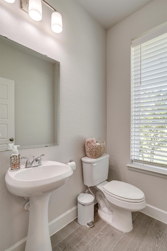 half bathroom with toilet, baseboards, and wood finished floors