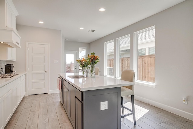 kitchen with white cabinets, light wood-style flooring, a kitchen island with sink, light countertops, and a sink