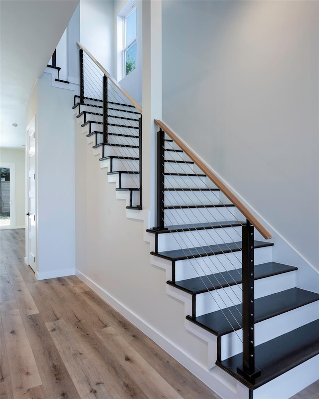 stairs featuring a towering ceiling, baseboards, and wood finished floors