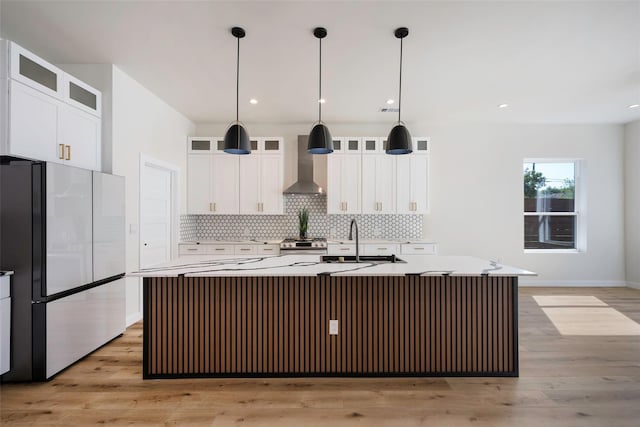 kitchen featuring stainless steel appliances, a sink, wall chimney exhaust hood, and tasteful backsplash