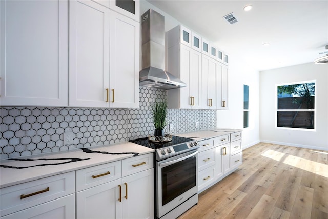 kitchen with visible vents, white cabinets, wall chimney exhaust hood, light wood-type flooring, and stainless steel range with electric stovetop