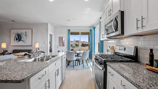 kitchen with stainless steel appliances, decorative backsplash, open floor plan, white cabinets, and a sink