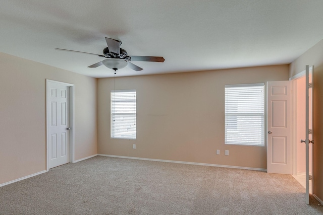 carpeted spare room with a ceiling fan and baseboards