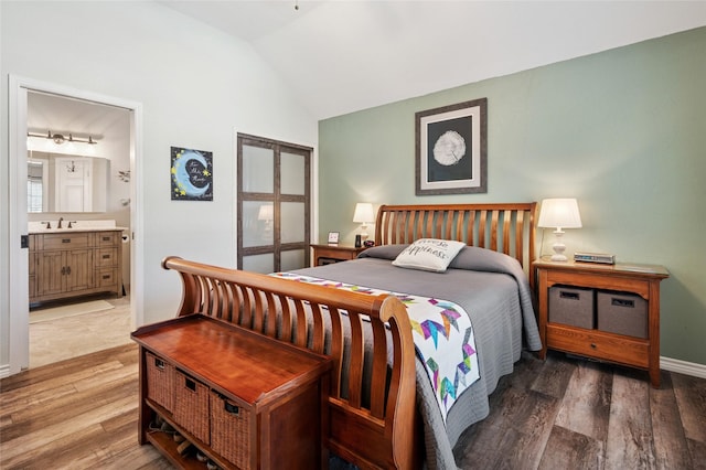 bedroom featuring baseboards, connected bathroom, wood finished floors, vaulted ceiling, and a sink