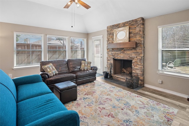 living area featuring lofted ceiling, a stone fireplace, wood finished floors, a ceiling fan, and baseboards