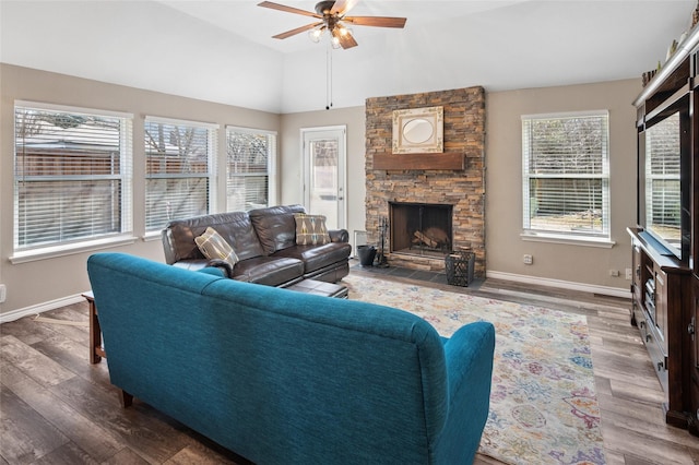 living area featuring vaulted ceiling, a stone fireplace, wood finished floors, and baseboards