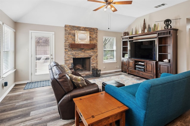 living area featuring visible vents, vaulted ceiling, a stone fireplace, and wood finished floors