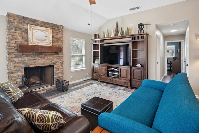 living area featuring visible vents, vaulted ceiling, a stone fireplace, wood finished floors, and baseboards