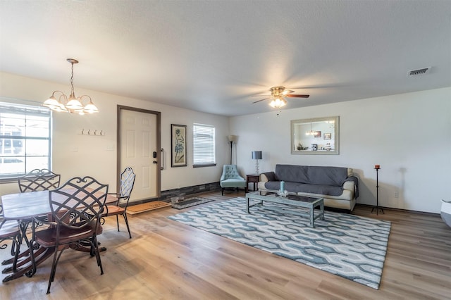 living room featuring visible vents, light wood-style flooring, a textured ceiling, and ceiling fan with notable chandelier