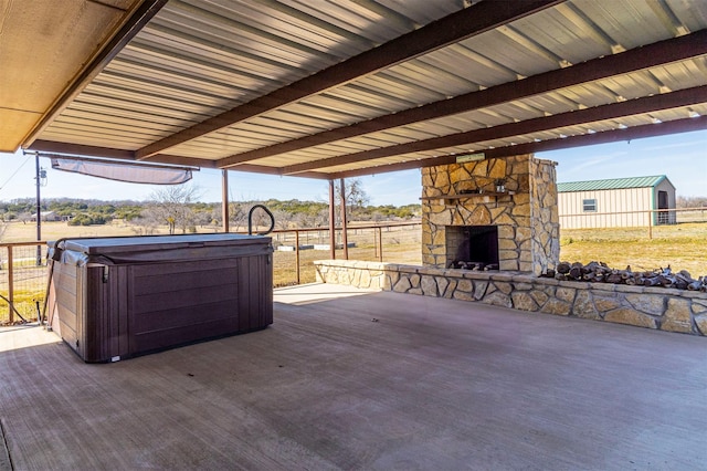 view of patio with an outdoor stone fireplace, fence, and a hot tub