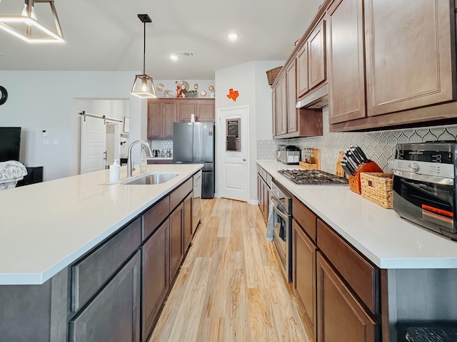 kitchen with a barn door, a sink, light wood-style floors, light countertops, and appliances with stainless steel finishes