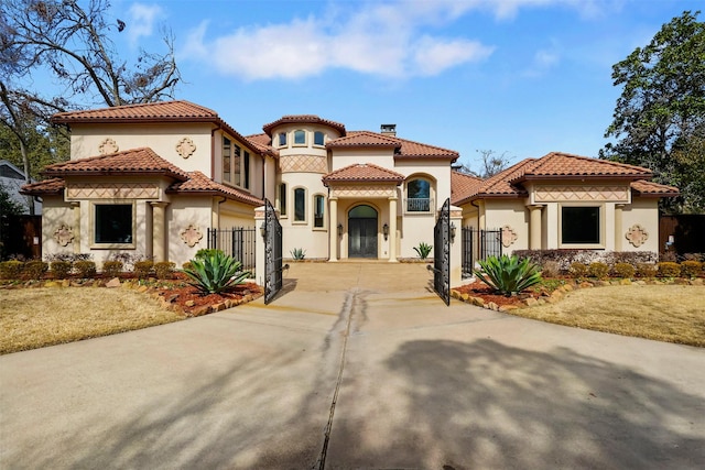 mediterranean / spanish house with a tile roof, a chimney, stucco siding, fence, and driveway