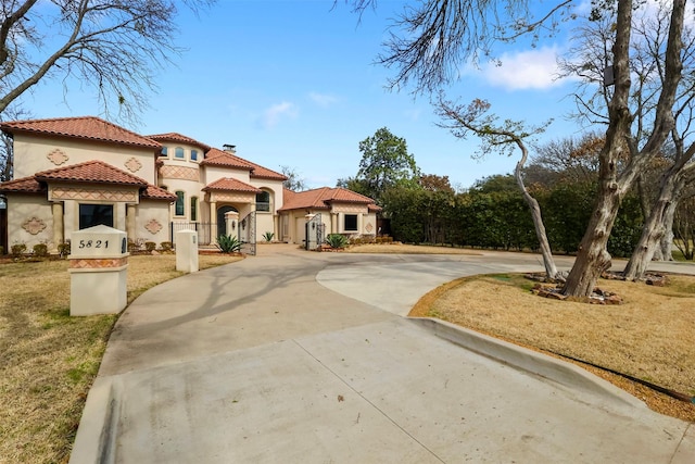 mediterranean / spanish-style home with a tile roof, driveway, a chimney, and stucco siding