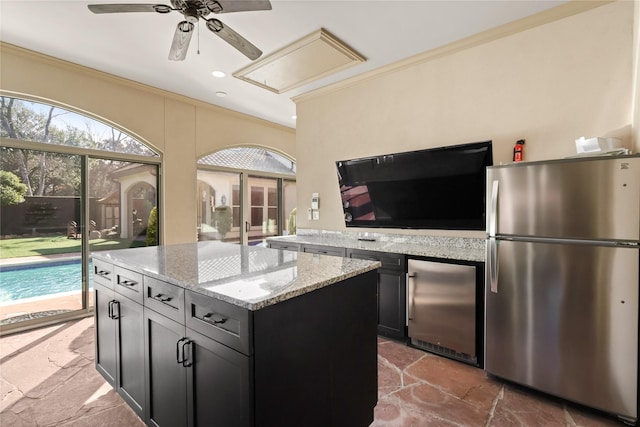 kitchen with stone tile floors, ornamental molding, stainless steel refrigerator, freestanding refrigerator, and light stone countertops