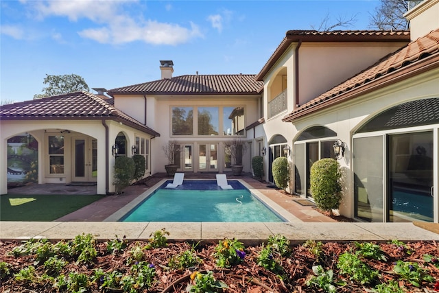 rear view of house featuring a tiled roof, french doors, a chimney, and stucco siding