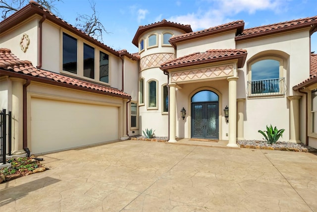 mediterranean / spanish-style home with a garage, driveway, a tiled roof, and stucco siding