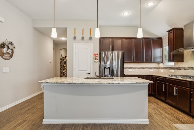 kitchen with stainless steel appliances, tasteful backsplash, a sink, wood finished floors, and wall chimney exhaust hood