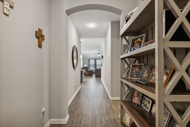 corridor featuring arched walkways, wood finished floors, and baseboards