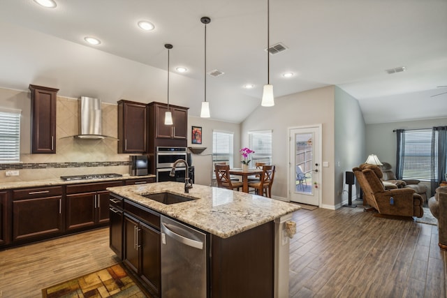 kitchen featuring lofted ceiling, visible vents, appliances with stainless steel finishes, a sink, and wall chimney exhaust hood