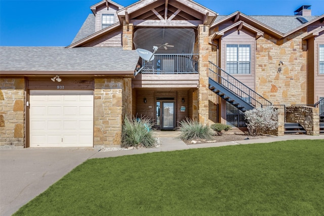 view of property with roof with shingles, stairway, a ceiling fan, a garage, and a front lawn