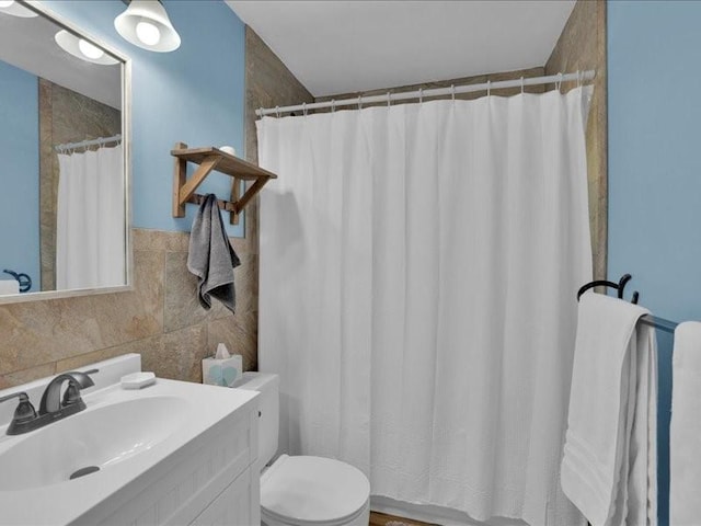 bathroom featuring toilet, curtained shower, vanity, and tile walls