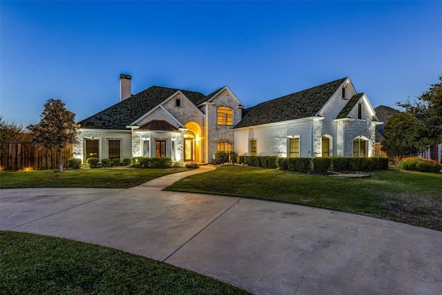 french country home featuring stone siding, a chimney, and a front lawn