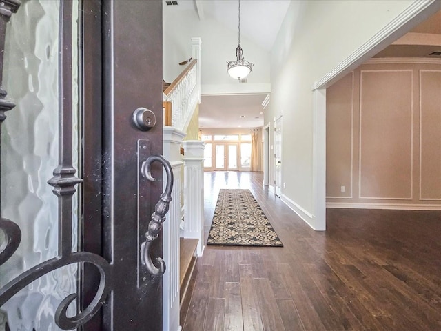 entryway featuring high vaulted ceiling, a decorative wall, baseboards, and wood finished floors