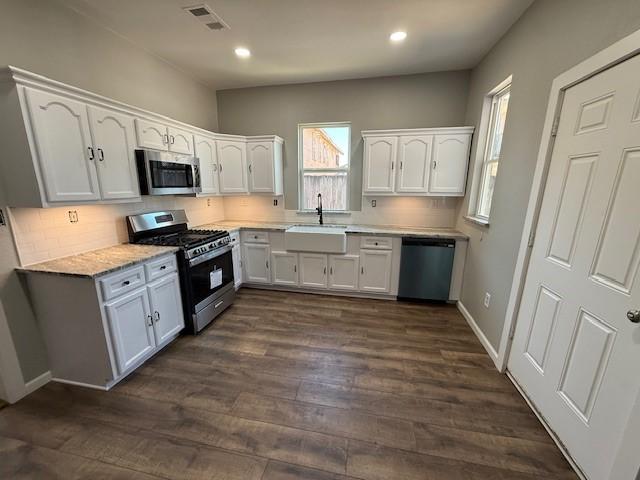 kitchen featuring stainless steel appliances, a sink, visible vents, white cabinetry, and dark wood-style floors