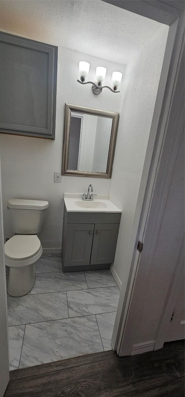 half bath with toilet, marble finish floor, baseboards, and vanity