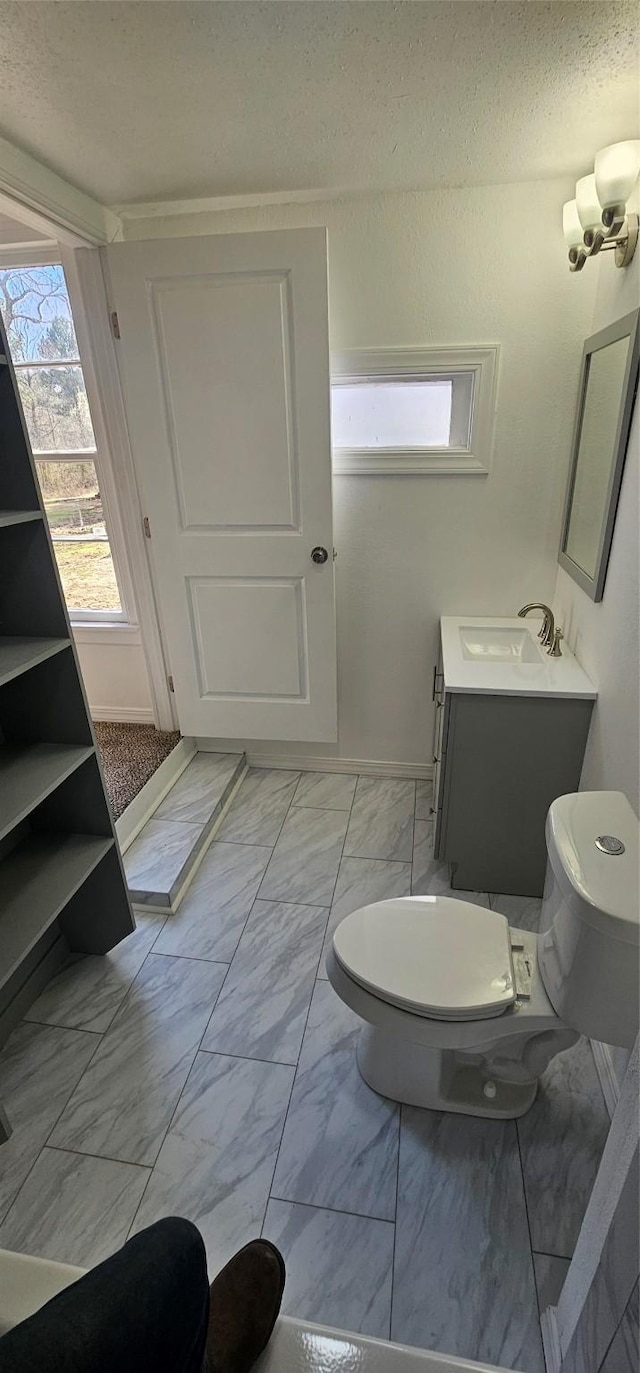 bathroom with toilet, marble finish floor, and vanity