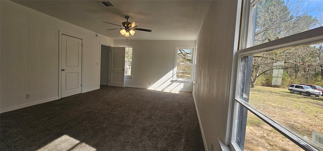 unfurnished room with a ceiling fan, visible vents, dark carpet, and baseboards