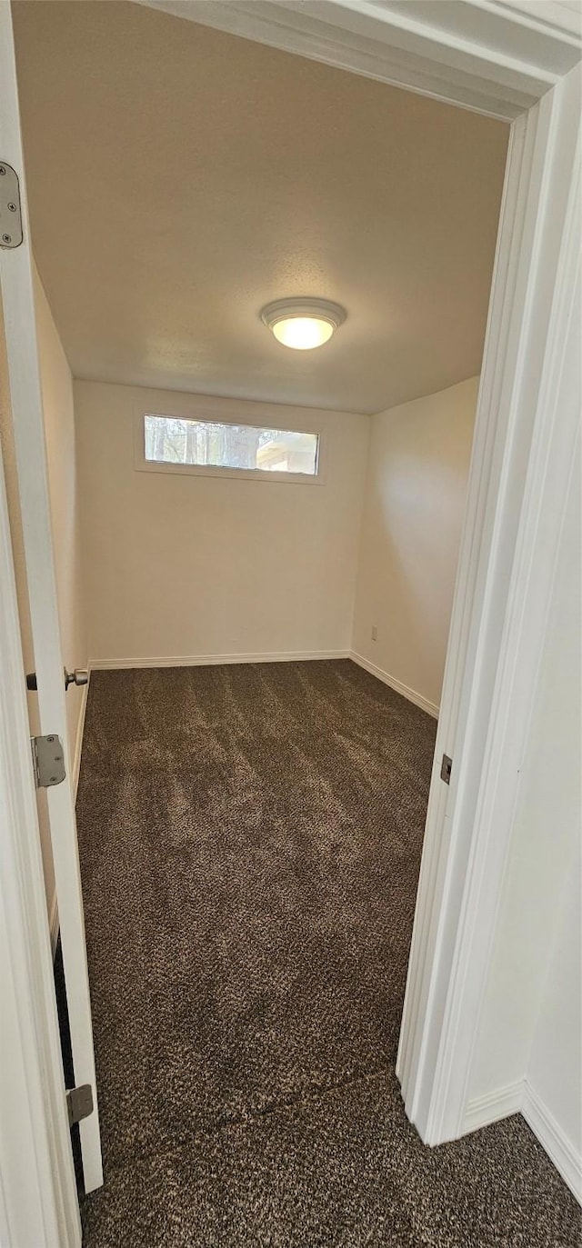 unfurnished room featuring dark carpet and baseboards