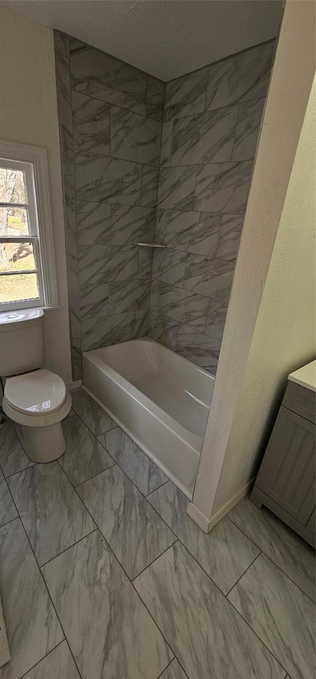 bathroom with marble finish floor, bathing tub / shower combination, toilet, vanity, and baseboards