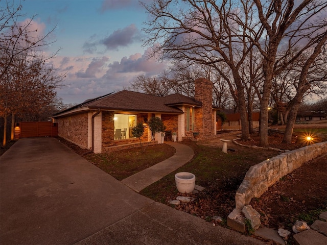 view of front of house with brick siding, a chimney, and fence