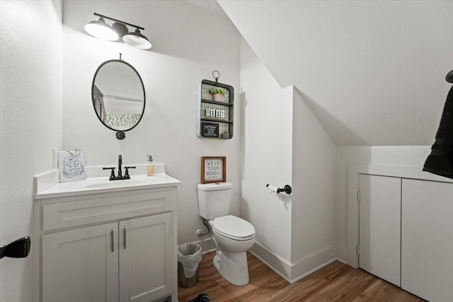 half bathroom featuring lofted ceiling, toilet, wood finished floors, vanity, and baseboards