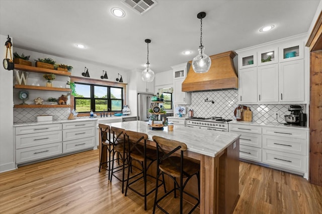 kitchen featuring premium appliances, visible vents, open shelves, light wood finished floors, and custom range hood