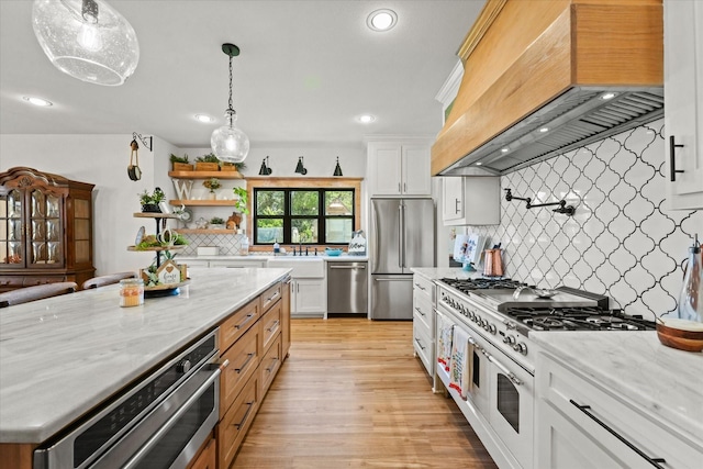 kitchen featuring premium appliances, light wood finished floors, custom exhaust hood, white cabinets, and light stone countertops