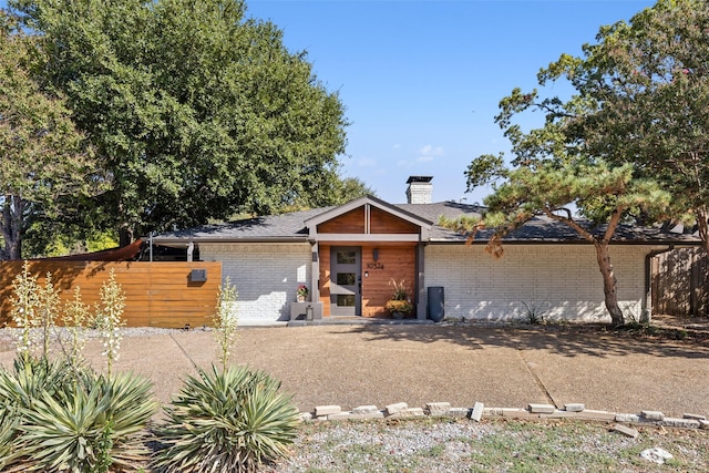 view of front of house with brick siding, a chimney, and fence