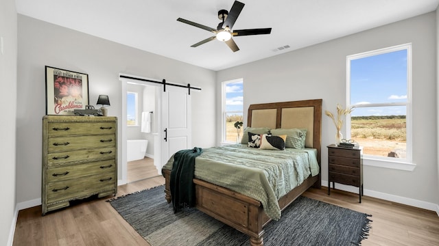 bedroom with light wood finished floors, a barn door, multiple windows, and visible vents