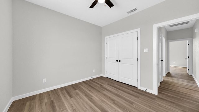 unfurnished bedroom with a closet, wood finished floors, visible vents, and baseboards