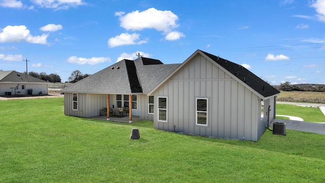 rear view of property featuring a shingled roof, a yard, central air condition unit, a patio area, and board and batten siding