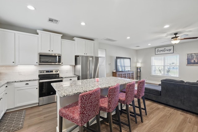 kitchen with light stone counters, stainless steel appliances, visible vents, light wood-type flooring, and decorative backsplash